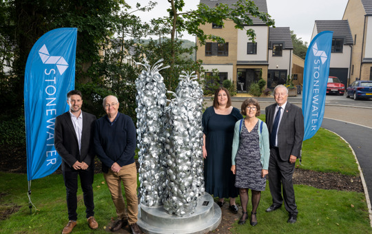 Employees, partners and artist in front of metal public art installation and Stonewater banners