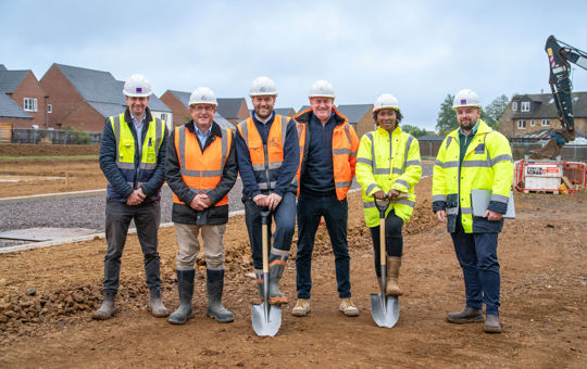 A row of people in protective clothing, two with spades on a construction site