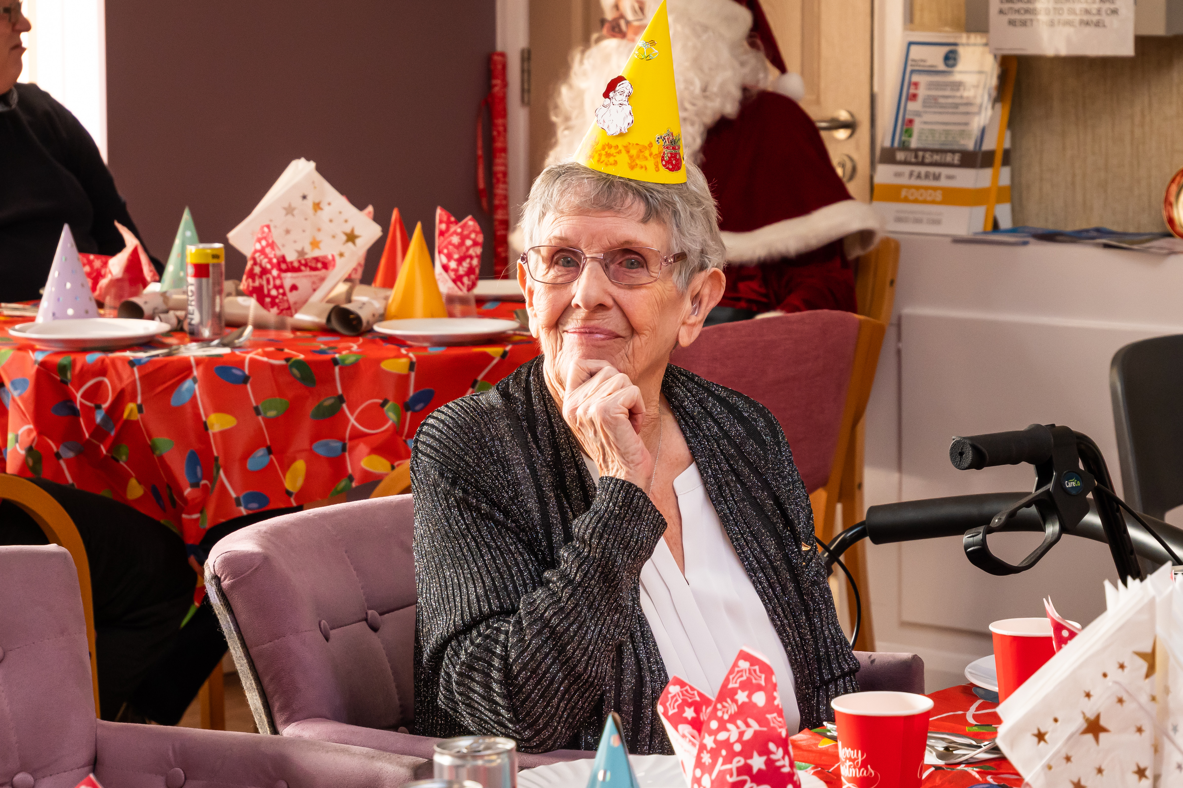 Smiling retirement living resident wearing party hat, sat at table with Christmas decorations 