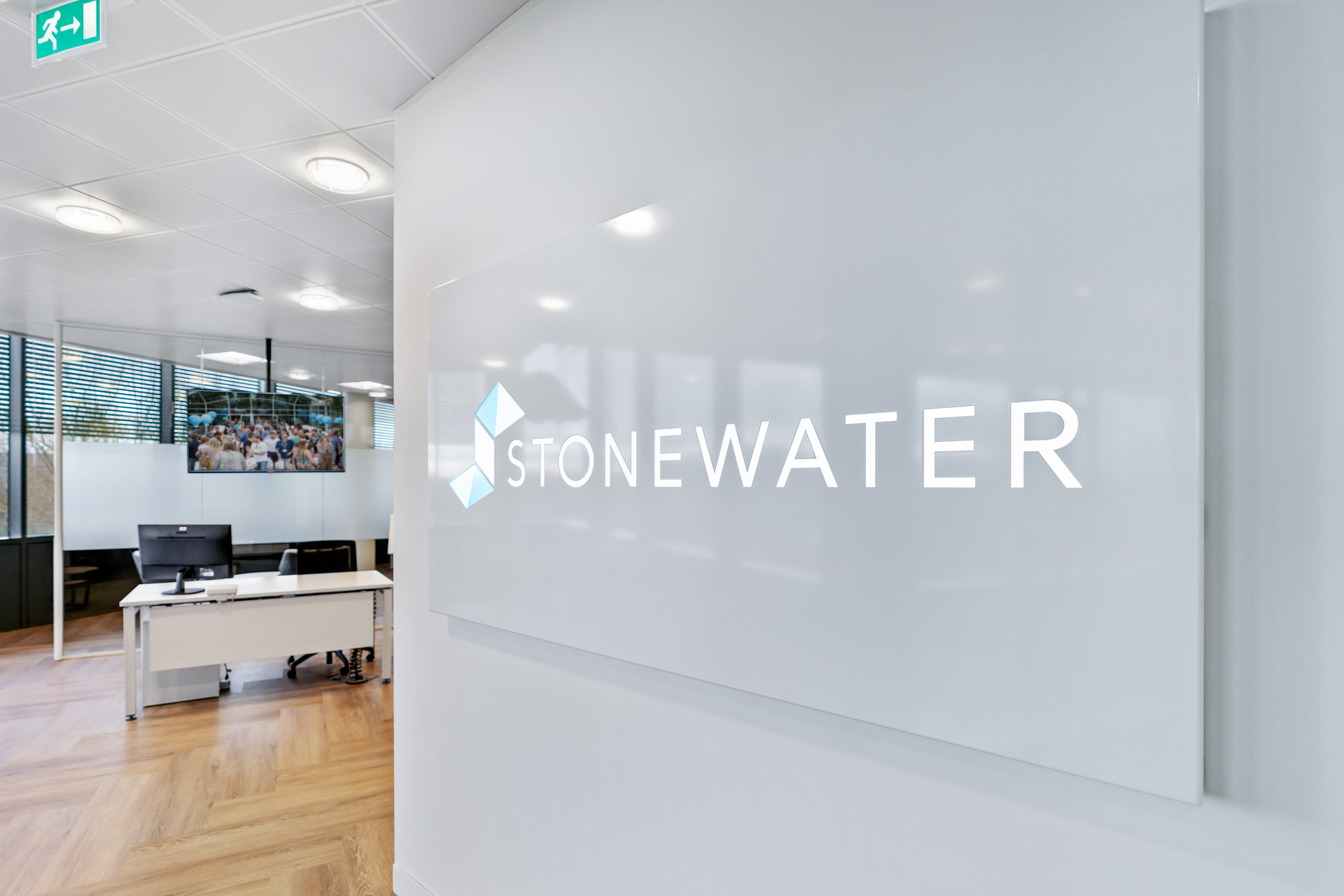 Close-up of Stonewater logo on glass panel in office, with reception desk in background
