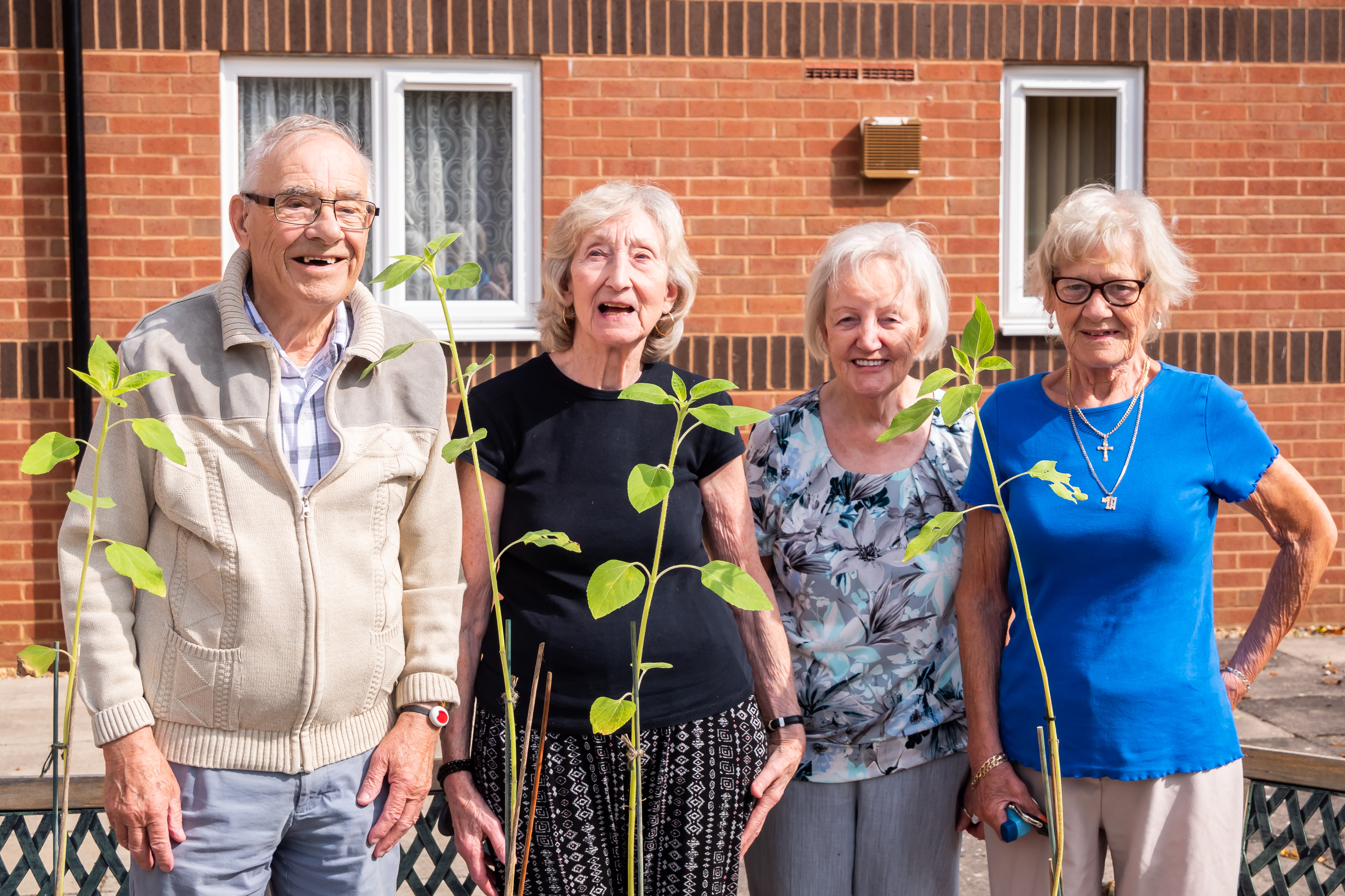 Four elderly residents stood outside retirement living scheme in front of plants