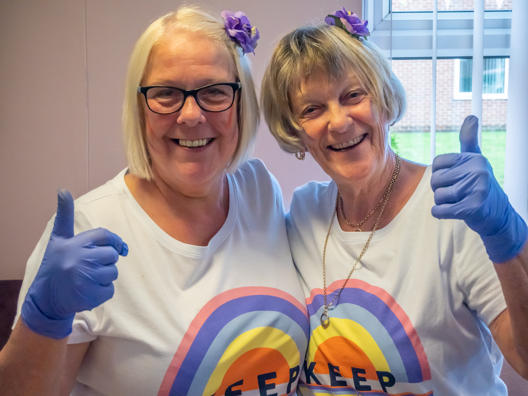 Two smiling residents at retirement living scheme wearing Pride t-shirts and blue surgical gloves