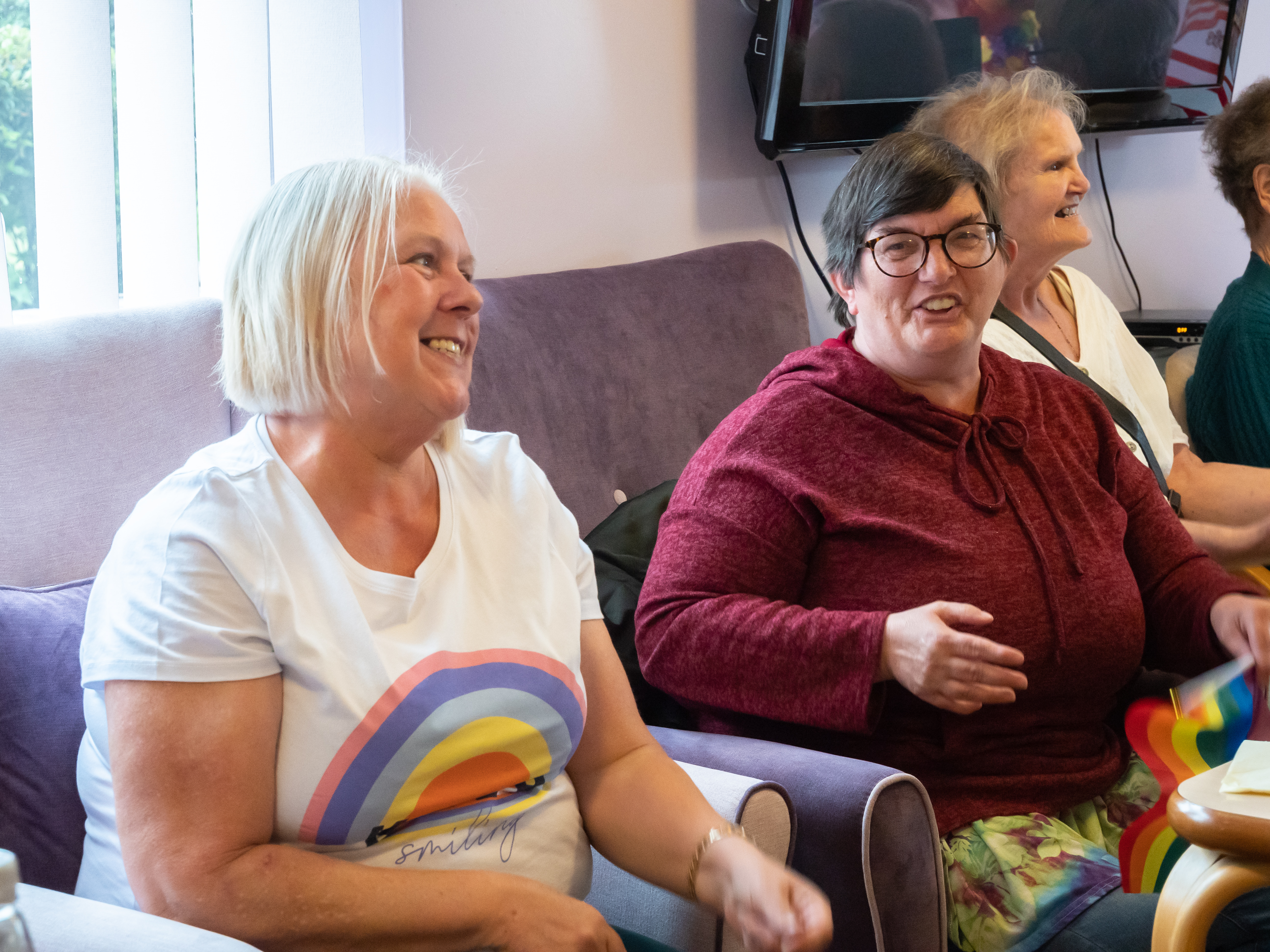 Two smiling residents sitting, one wearing Pride t-shirt and one holding pride flag