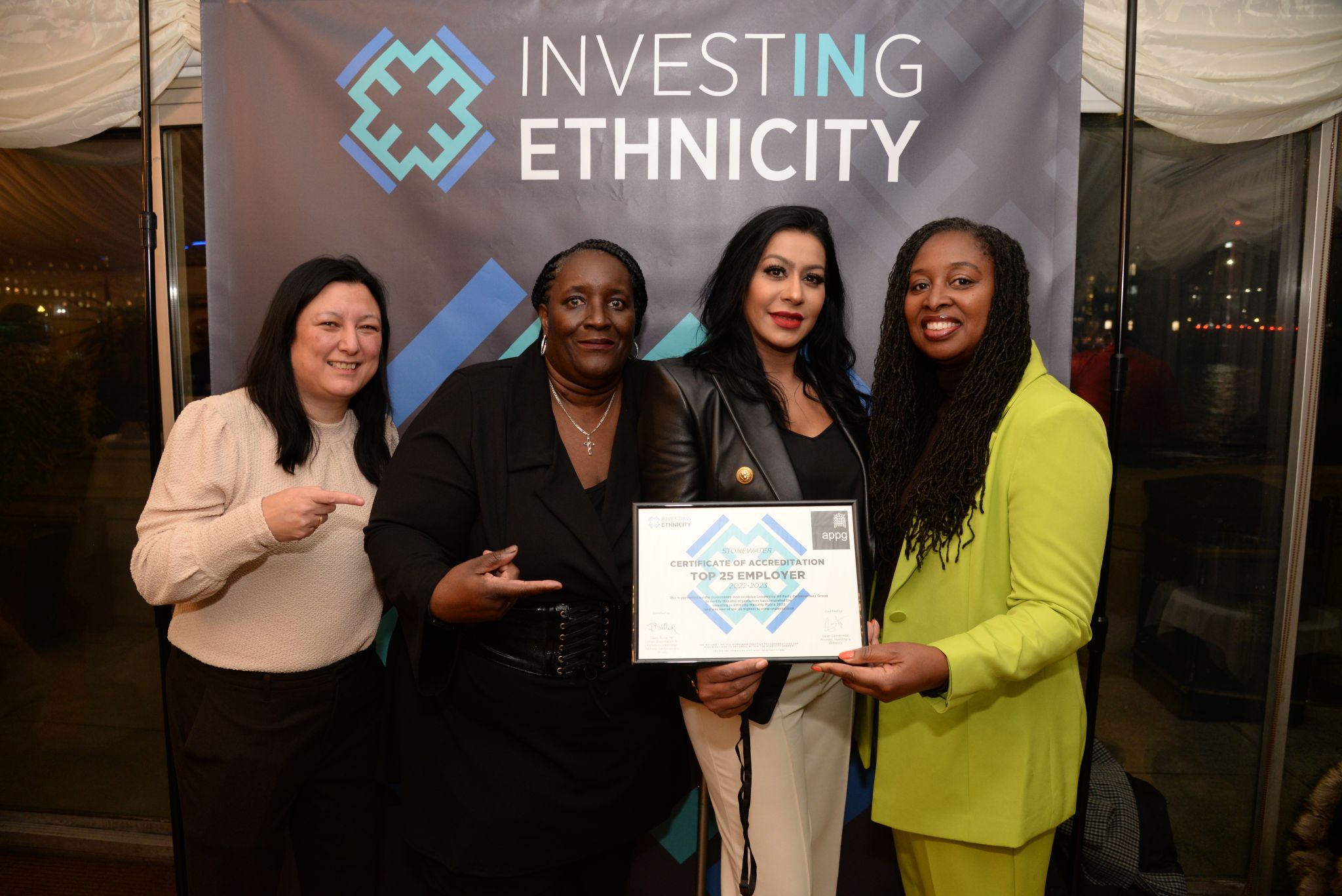 Four female Stonewater colleagues holding and pointing to award at ceremony