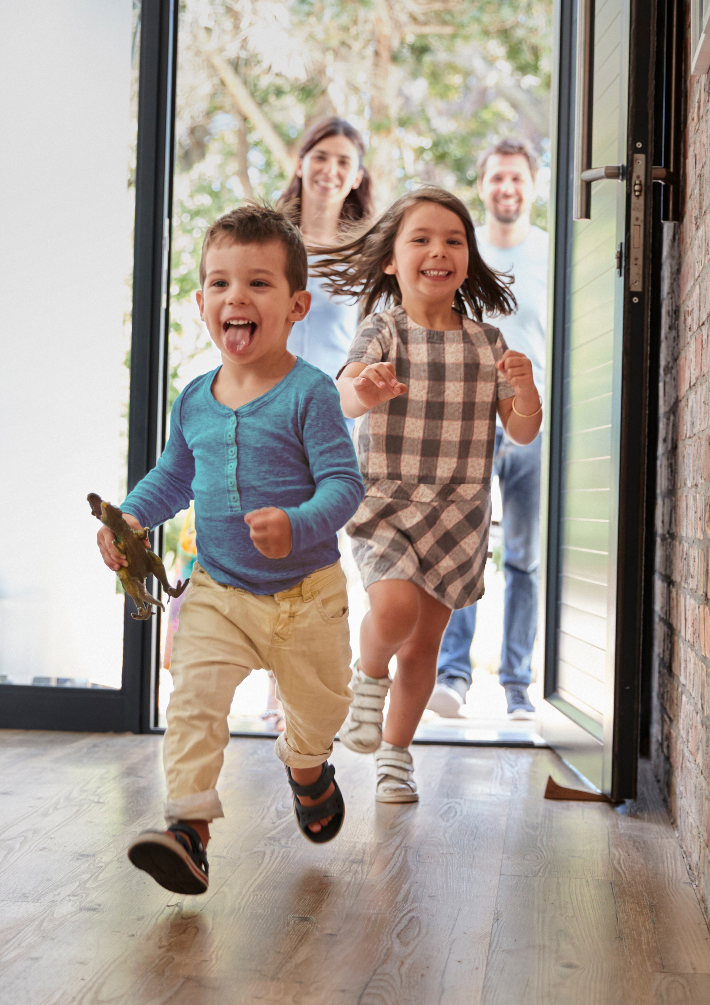 Two young children smiling and running into house, parents walking through doorway behind them