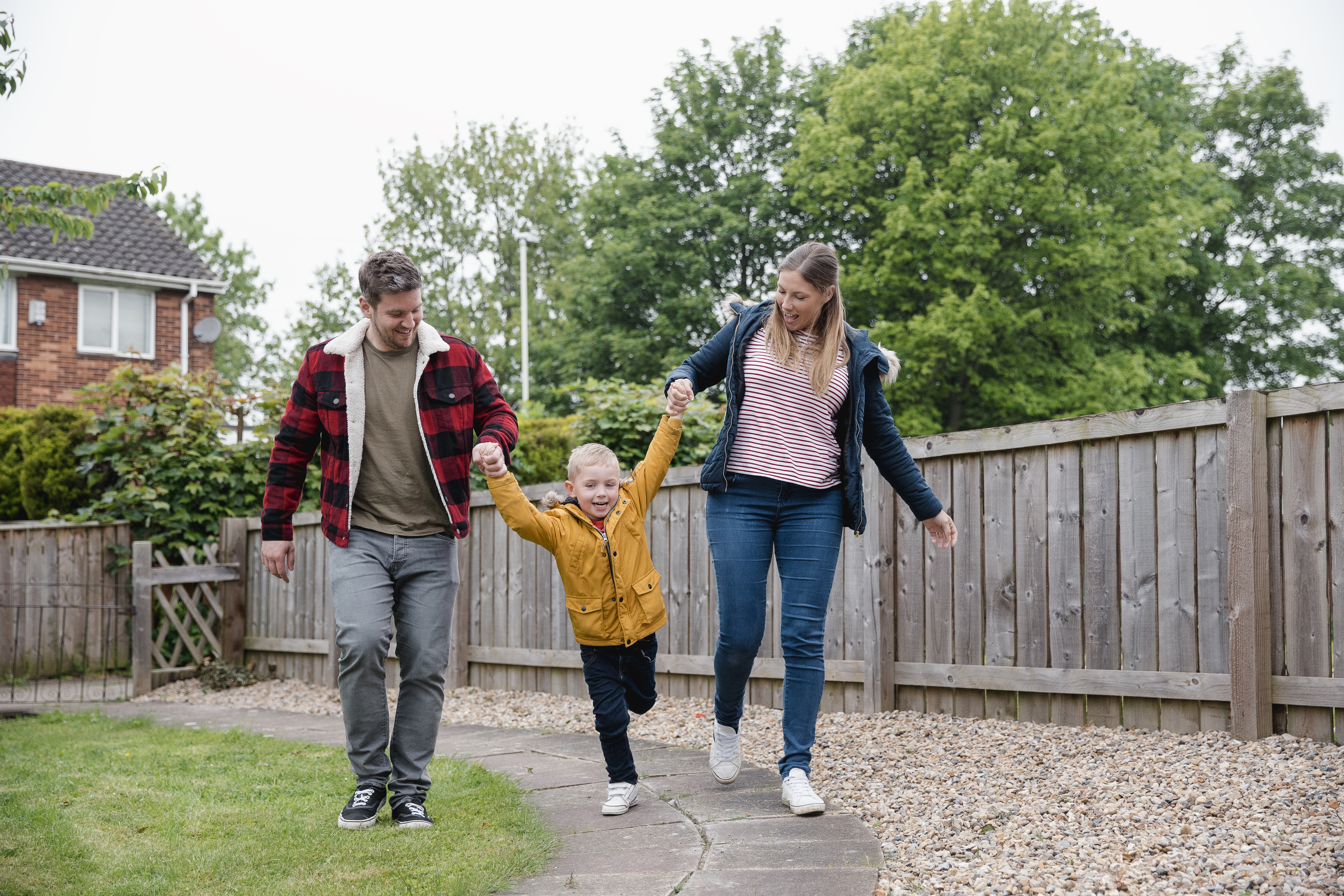 Mother and father walking down garden path swinging their son in between them