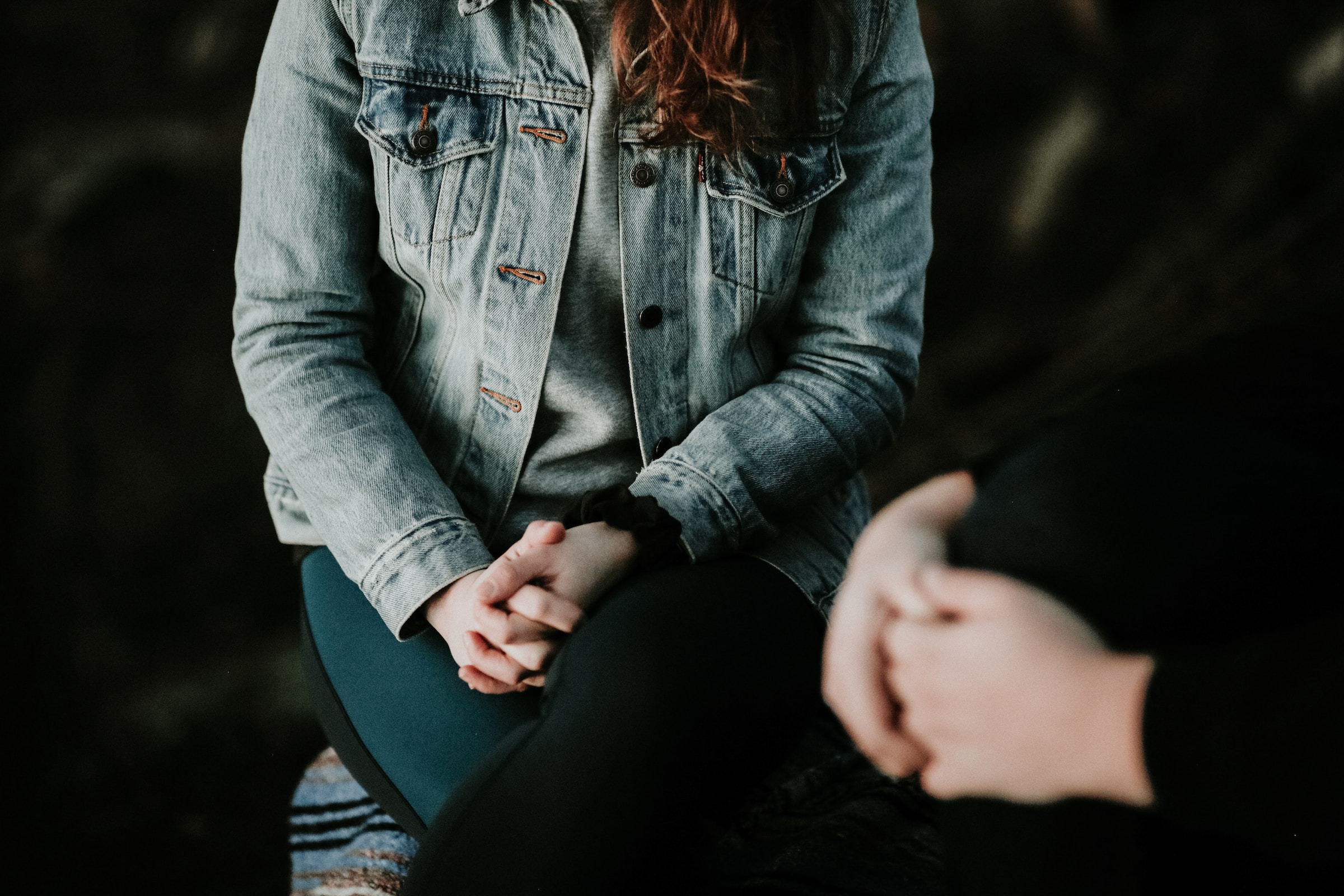 Woman in dark room sat cross legged holding her hands together, head out of shot