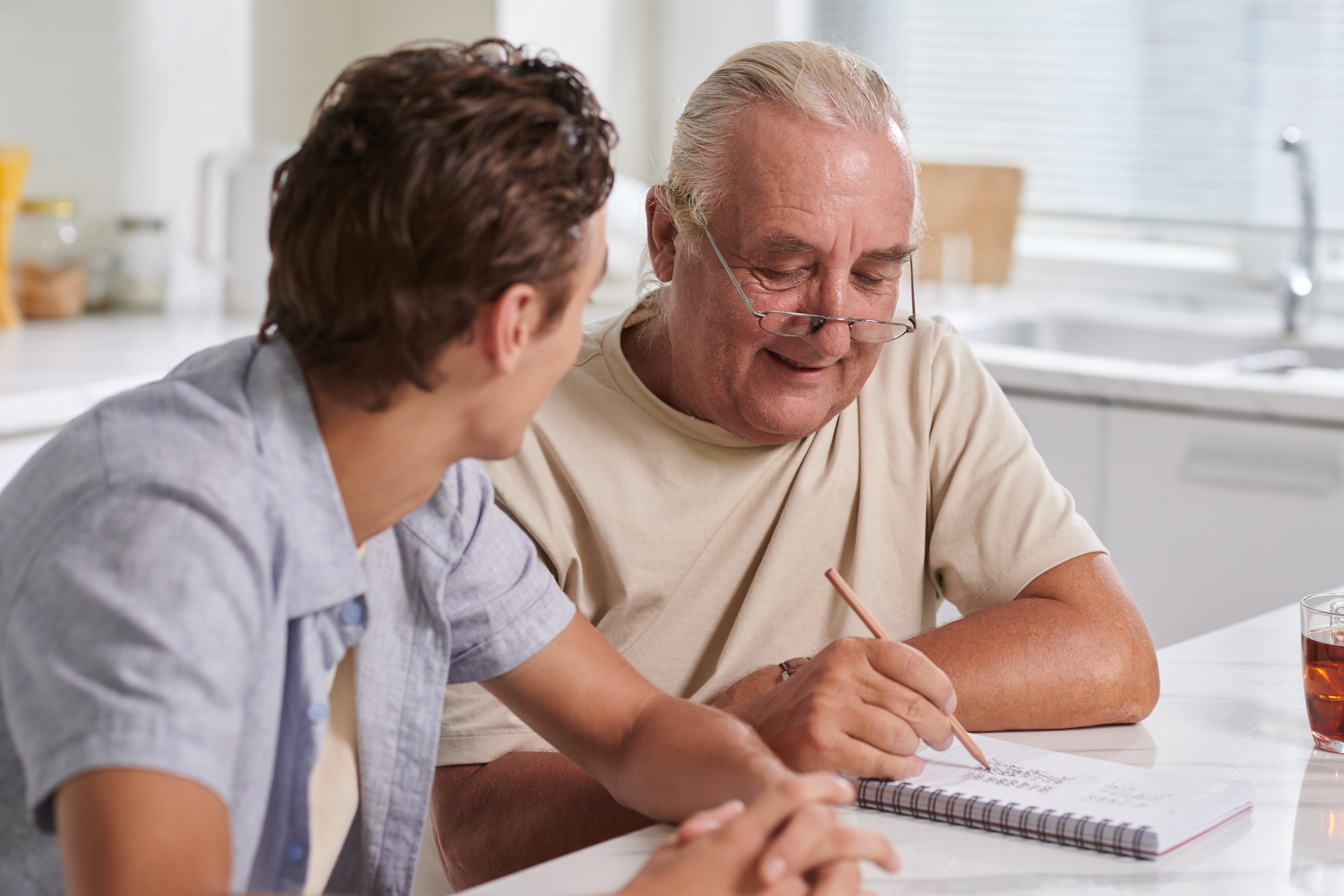 Young man sat talking to older man who is writing on a notepad