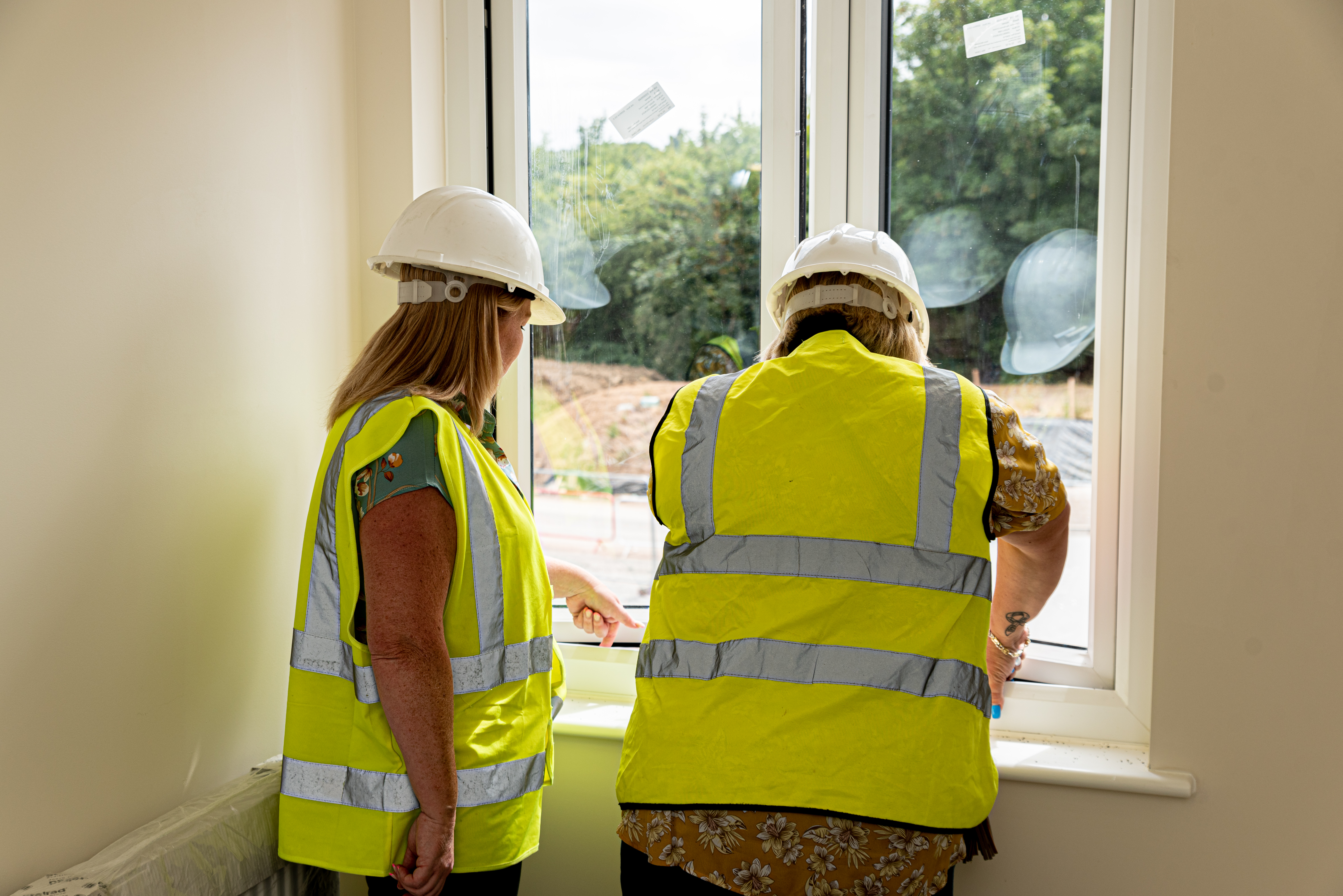 Two contractors looking out of window, wearing hi-vis jackets