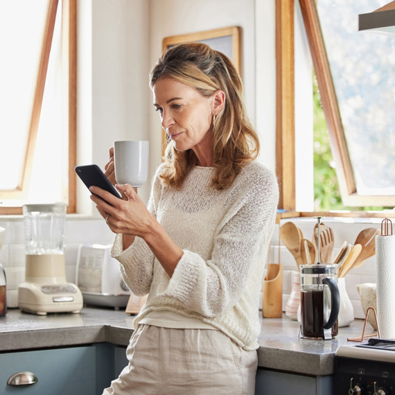 A woman stood looking at her phone with a mug in her hand.
