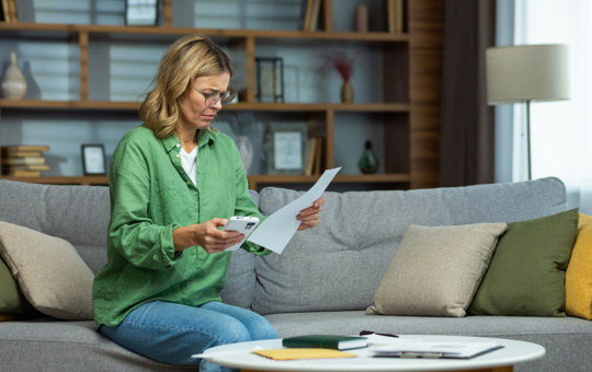 Blonde woman on sofa looking at paperwork in her hand with concerned expression
