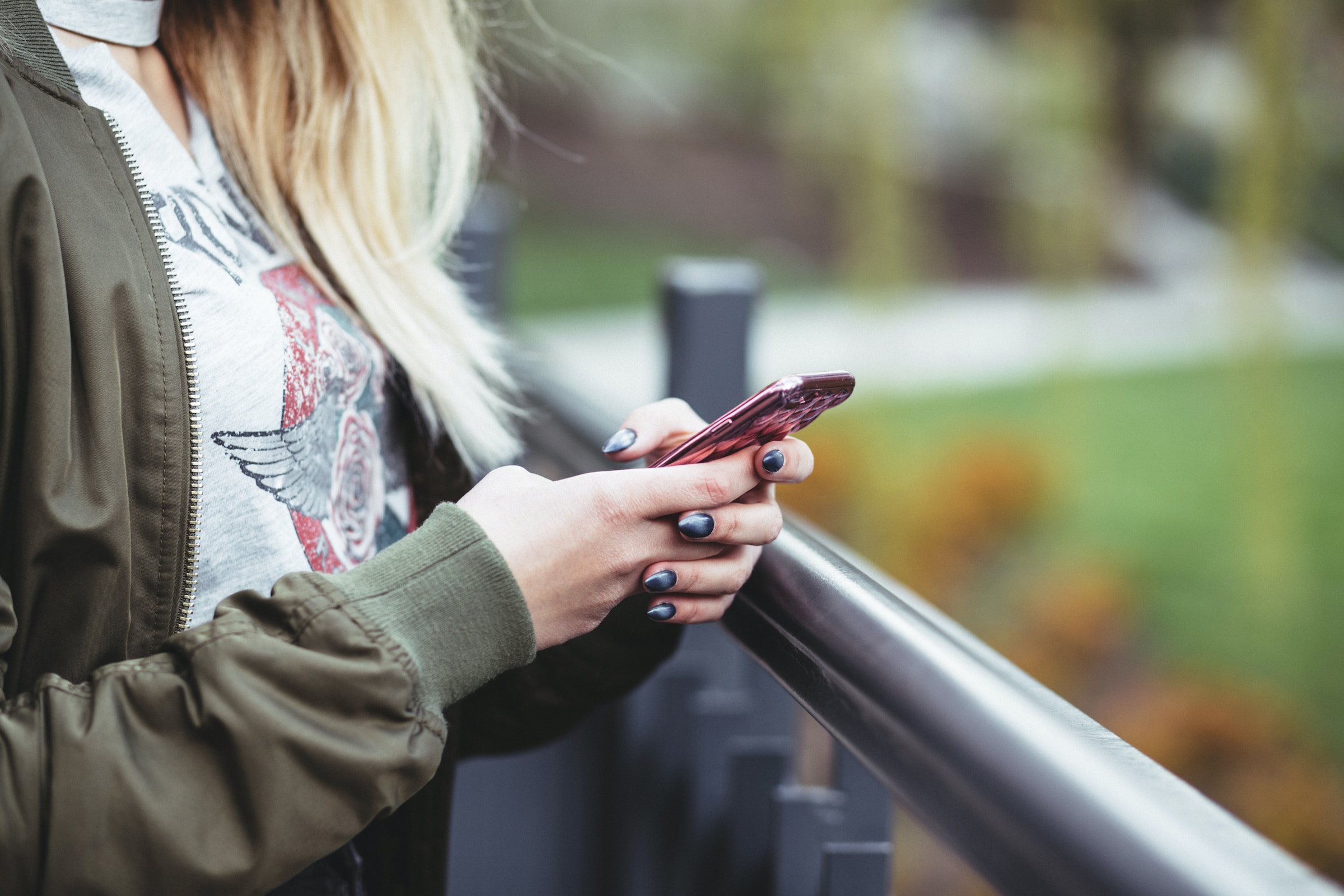 Lady stood outside near railing holding mobile phone in her hand