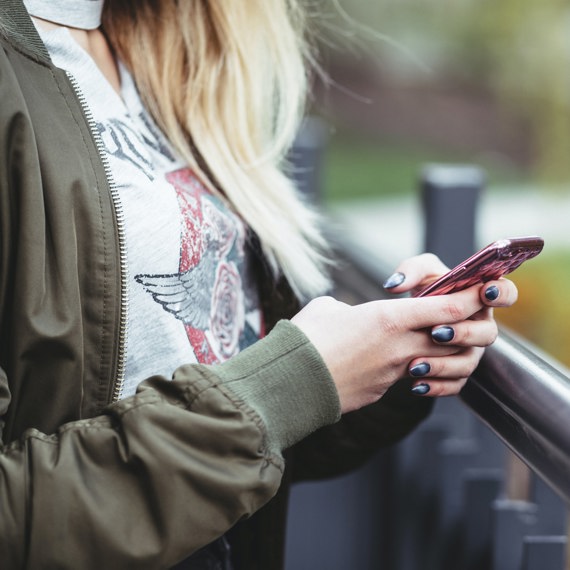 Lady stood outside near railing holding mobile phone in her hand