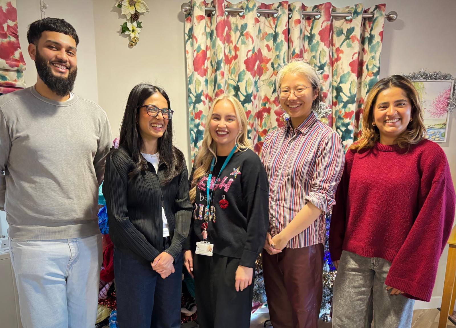 5 people stand posed for the camera. In the background are floral curtains and christmas decor