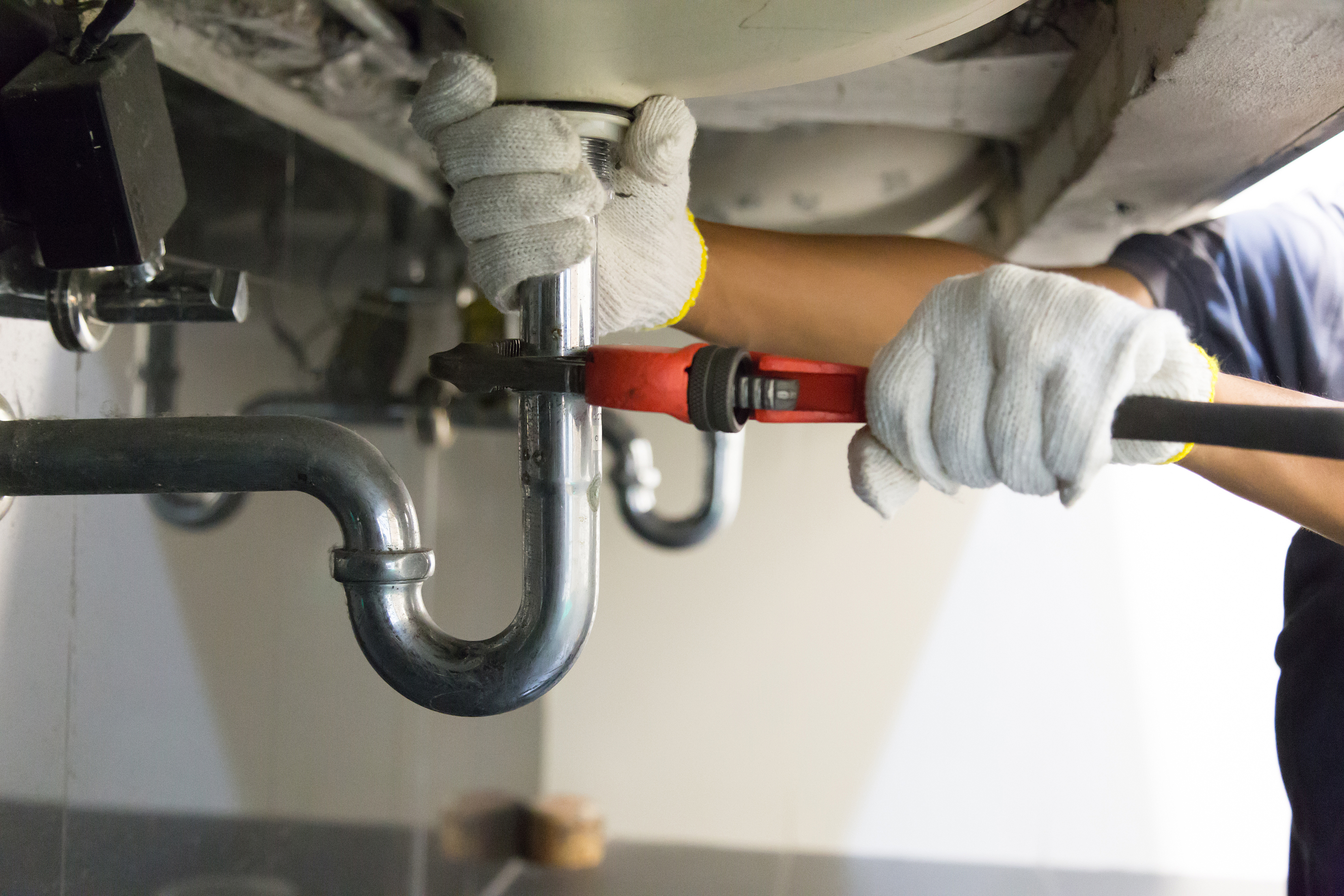 Close-up of plumber's hands in gloves using wrench on under-sink pipe