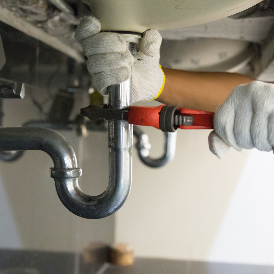 Close-up of plumber's hands in gloves using wrench on under-sink pipe