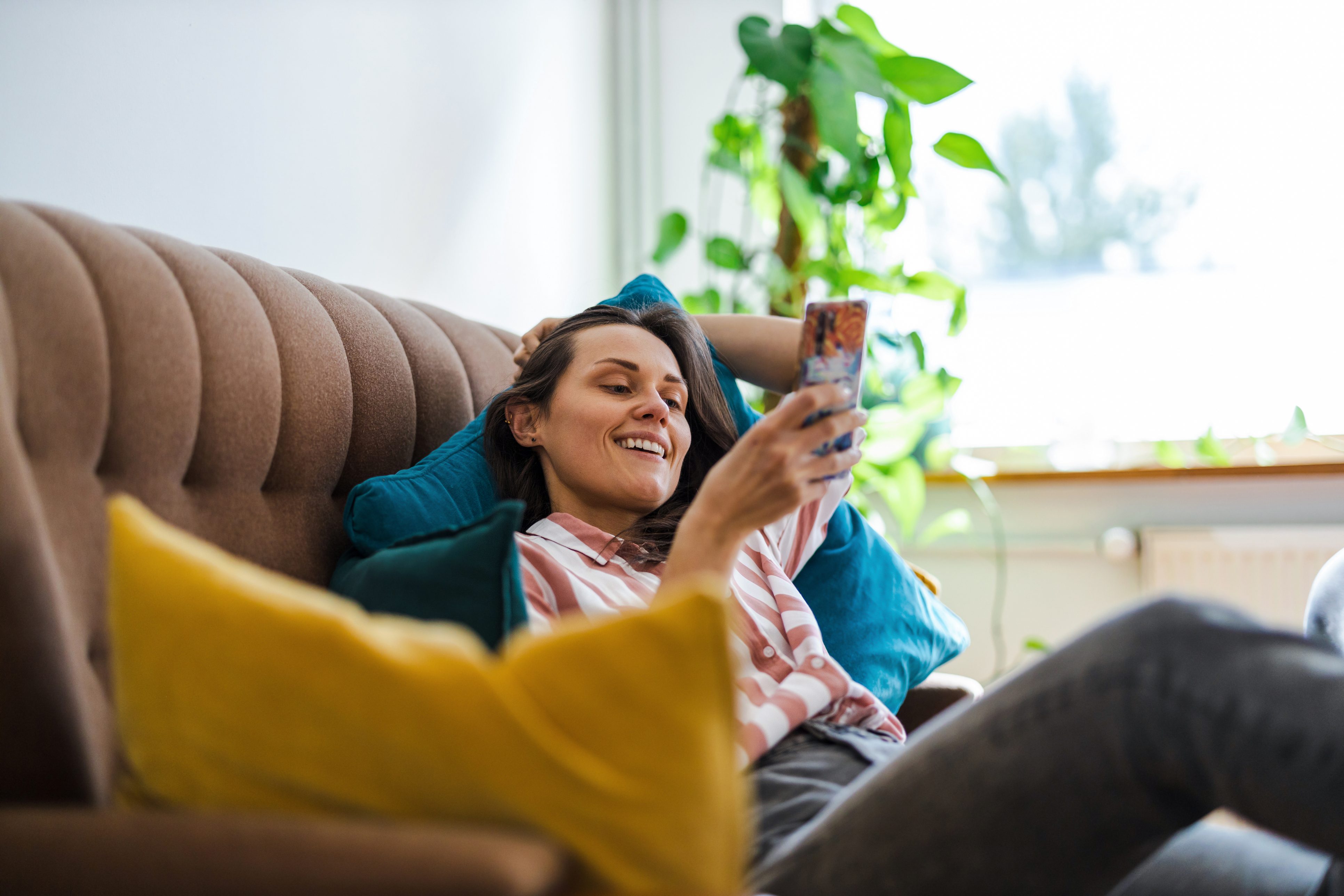 Lady slouched on sofa with legs up, smiling at the phone in her hand