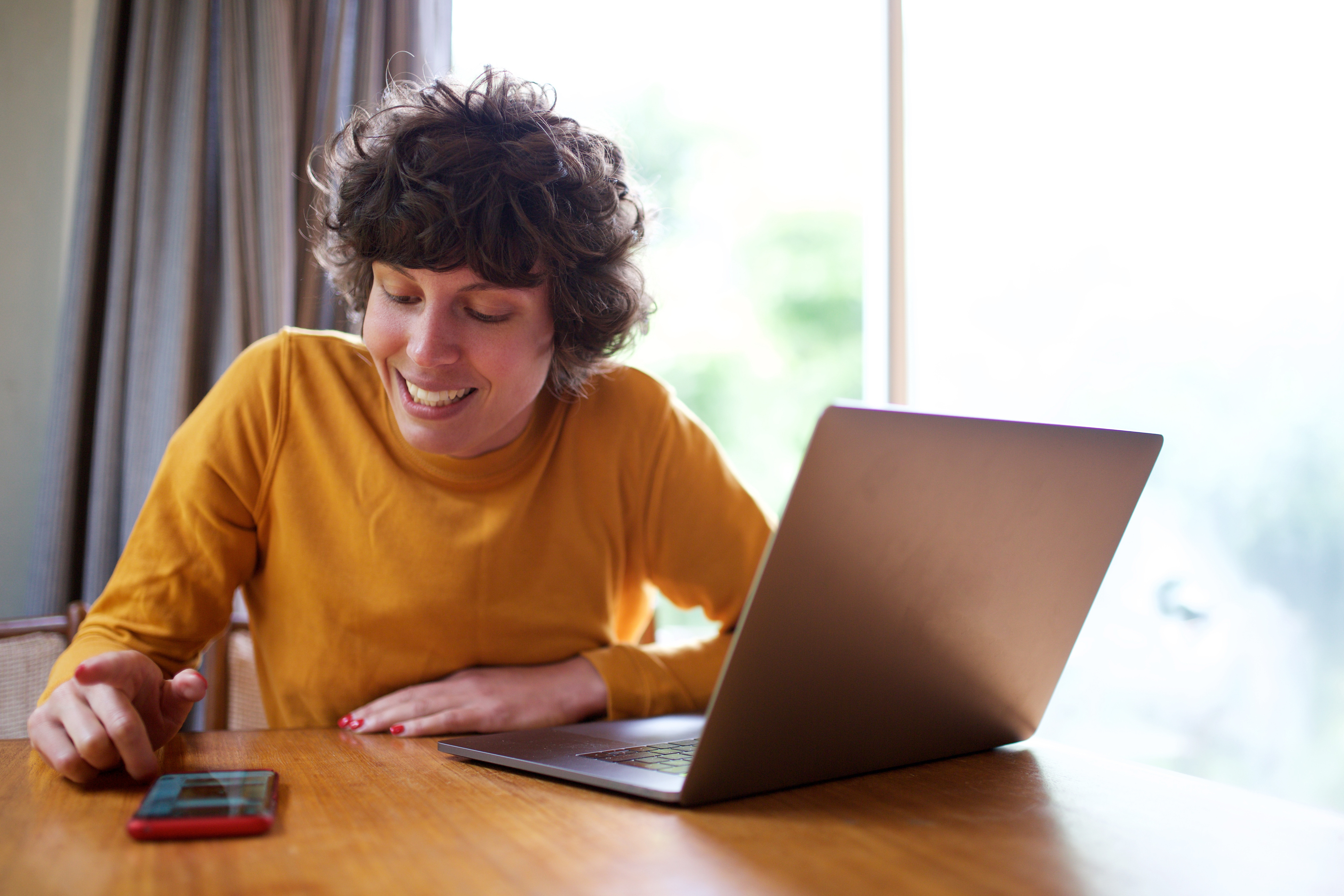 Lady in yellow jumper sat at table with laptop and phone in front of her