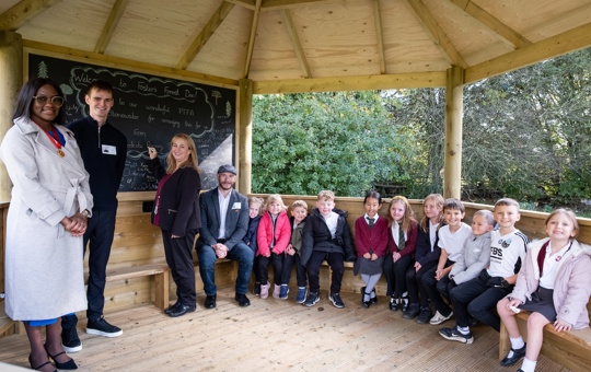 Group of children sat by a chalkboard with 4 adults