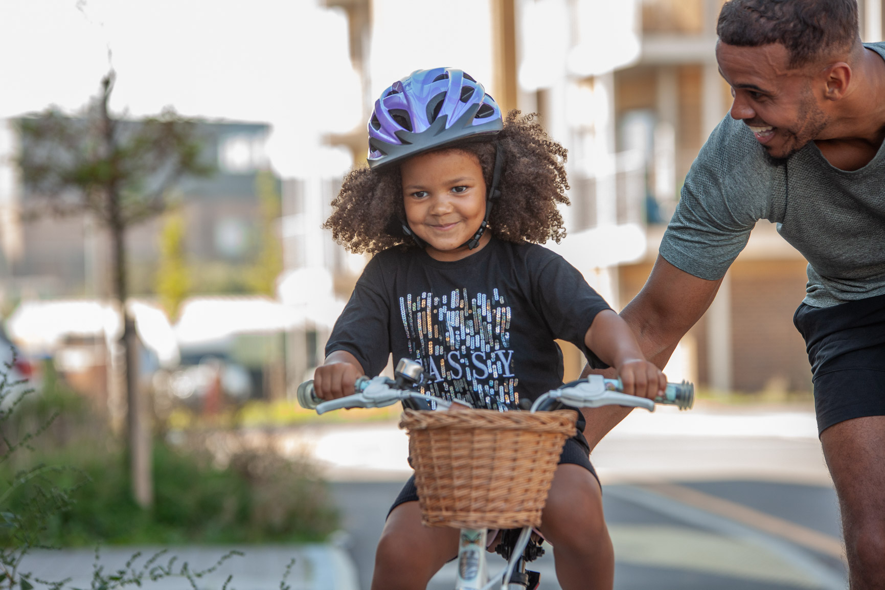 Young child riding bike, father is pushing behind