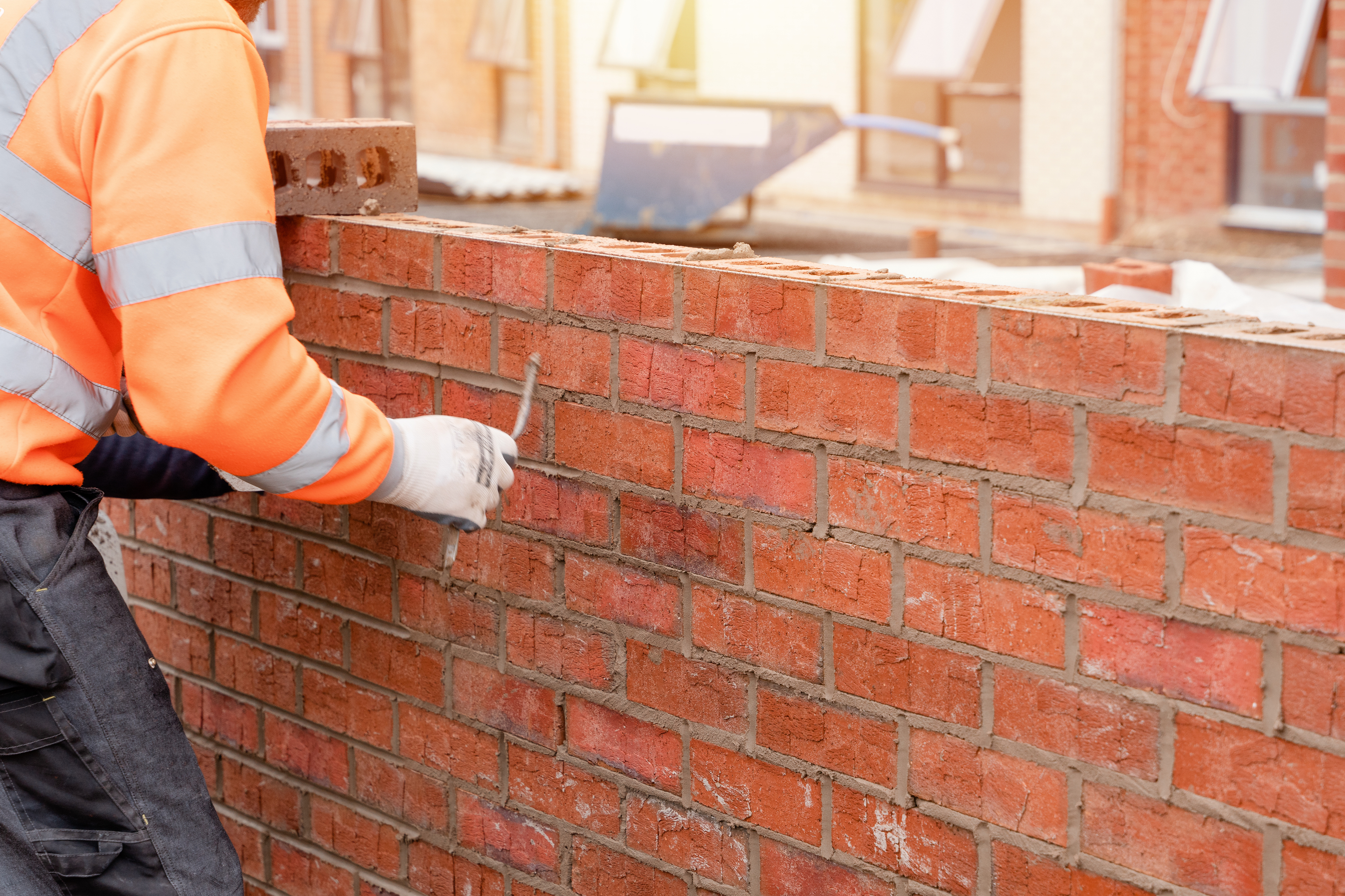 Close-up of man in hi-vis jacket laying bricks on a brick wall