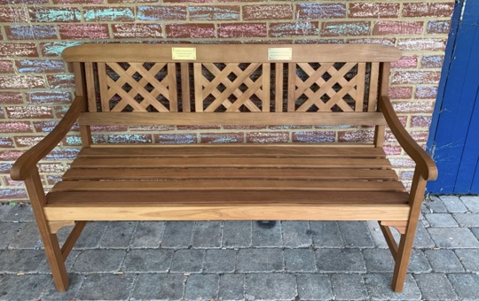 A wooden bench with inscribed gold coloured plaques on in front of brick wall