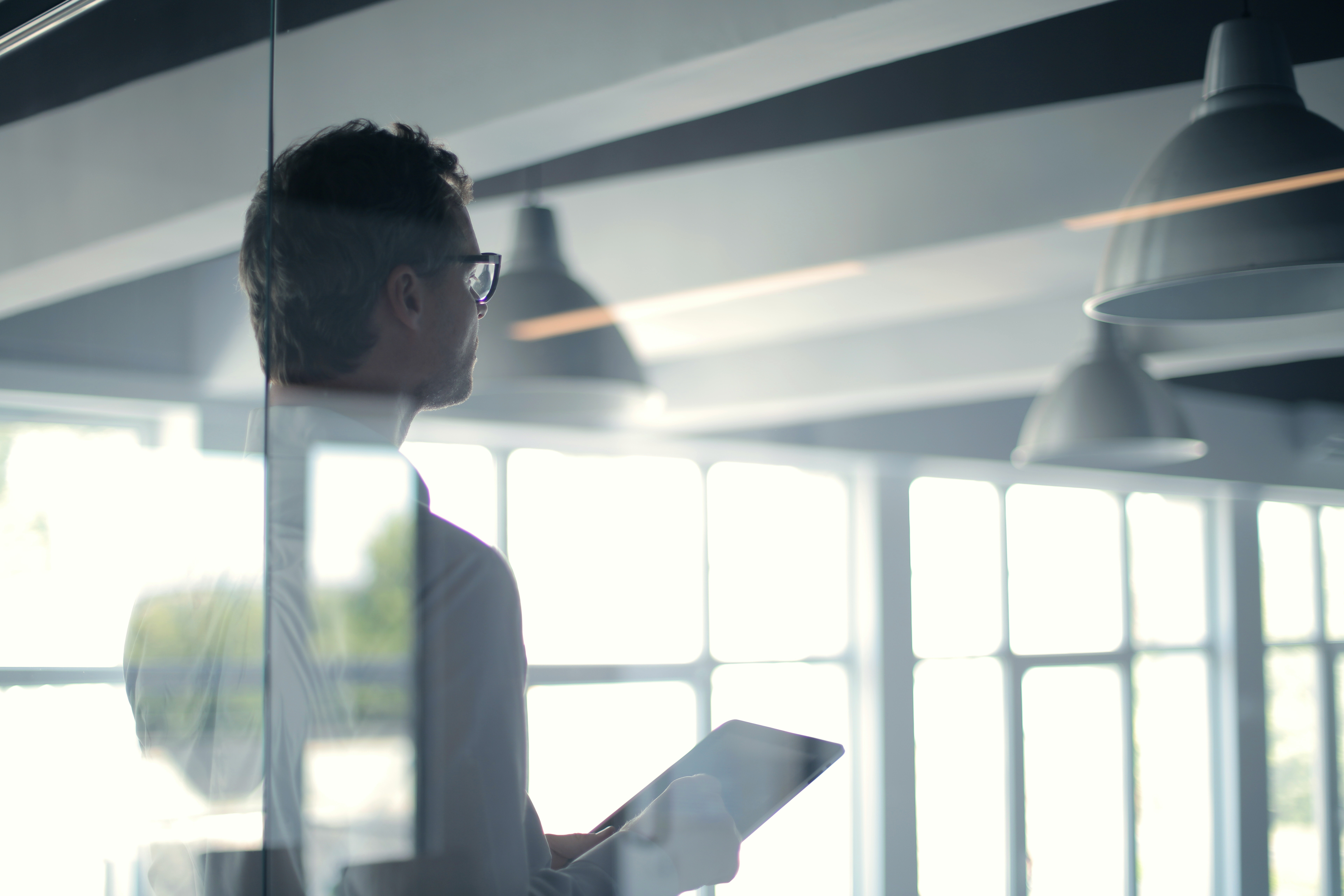 Man on tablet device in office, shot through the glass with light reflecting through the windows