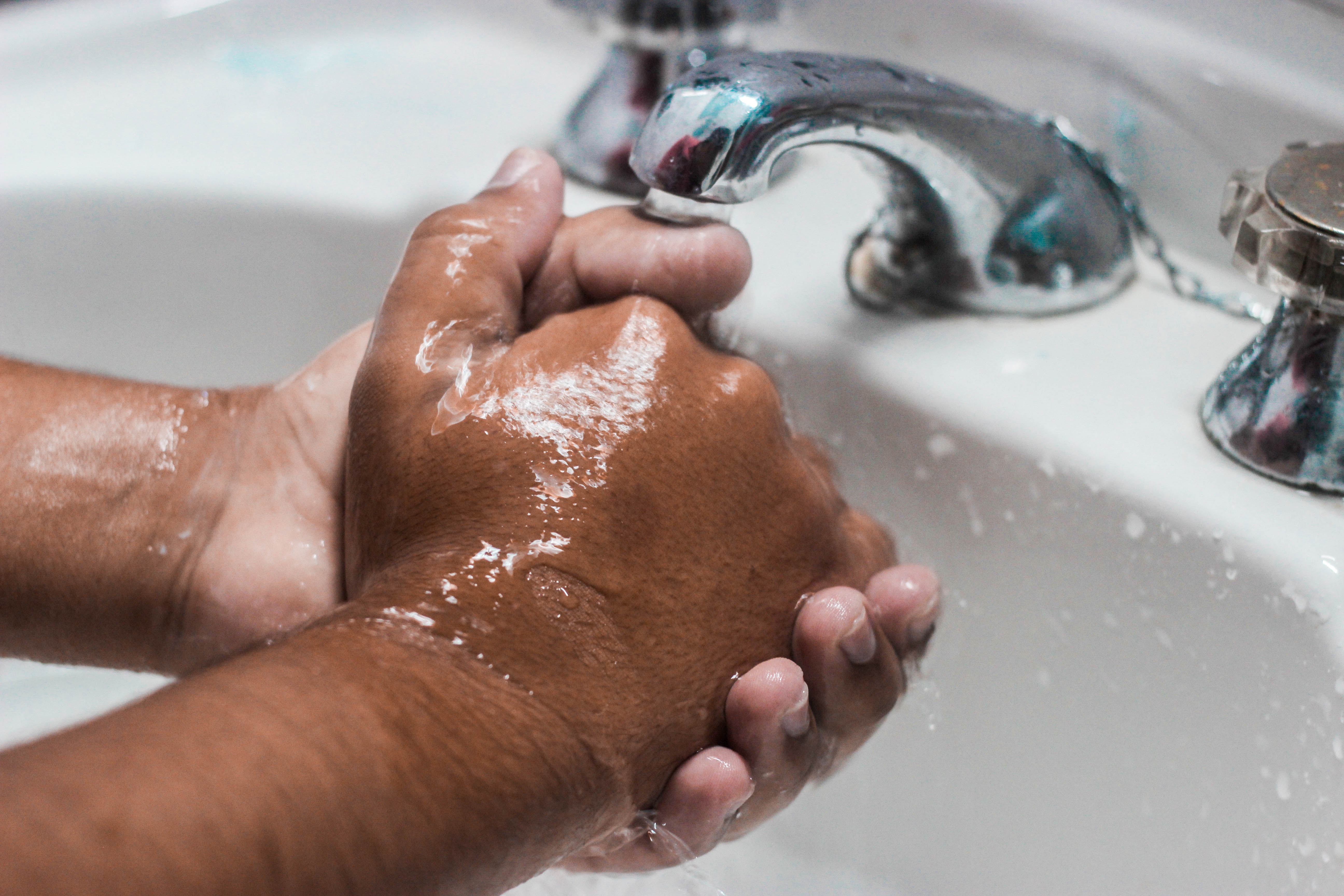 Close-up of a man washing his hands in a white sink