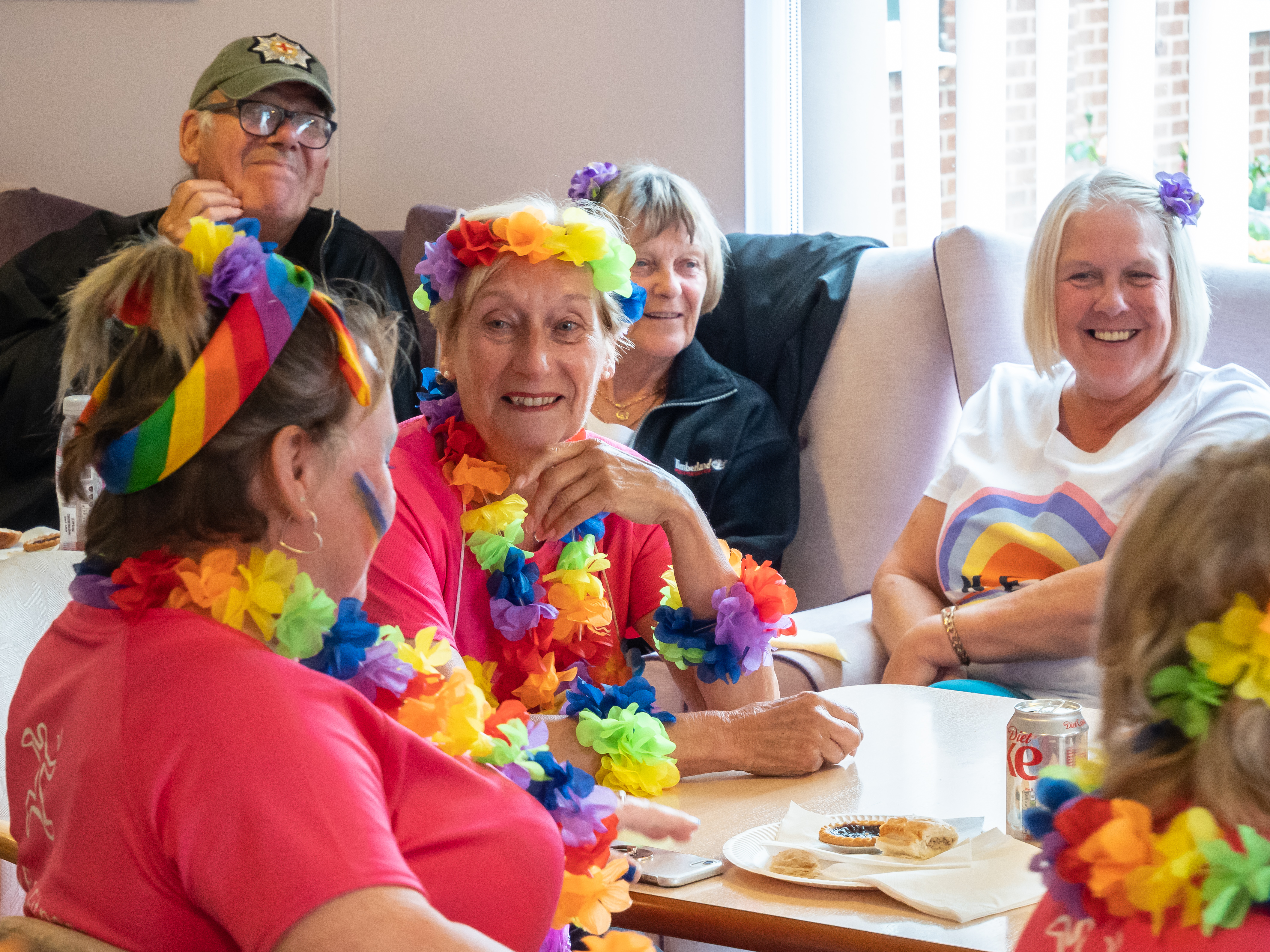 Six residents sat at table in retirement living scheme wearing floral necklaces to celebrate Pride