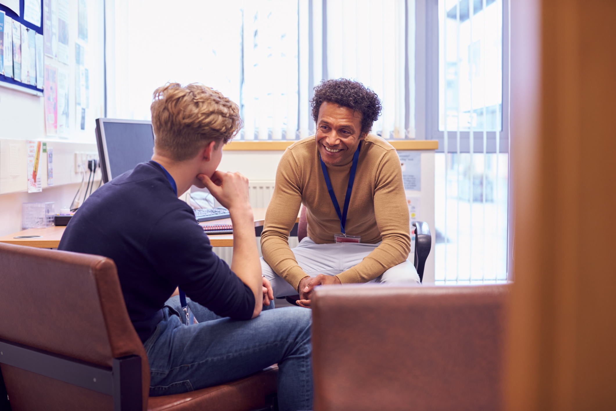 Mentor or coach sat in small office room talking to teenage boy