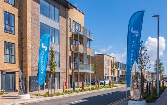 Sunny street scene of new-build apartments with blue Stonewater banners outside