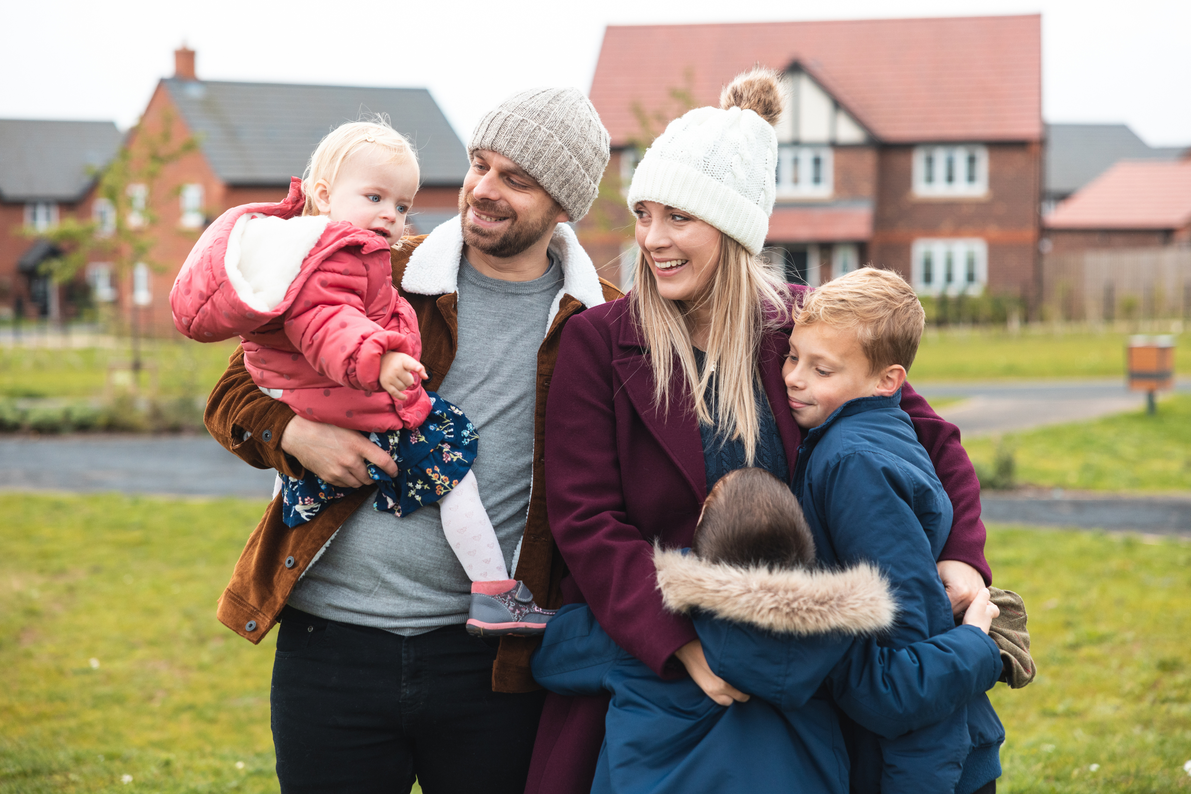 Young parents with two boys and baby in father's arms, stood in front of a new-build scheme
