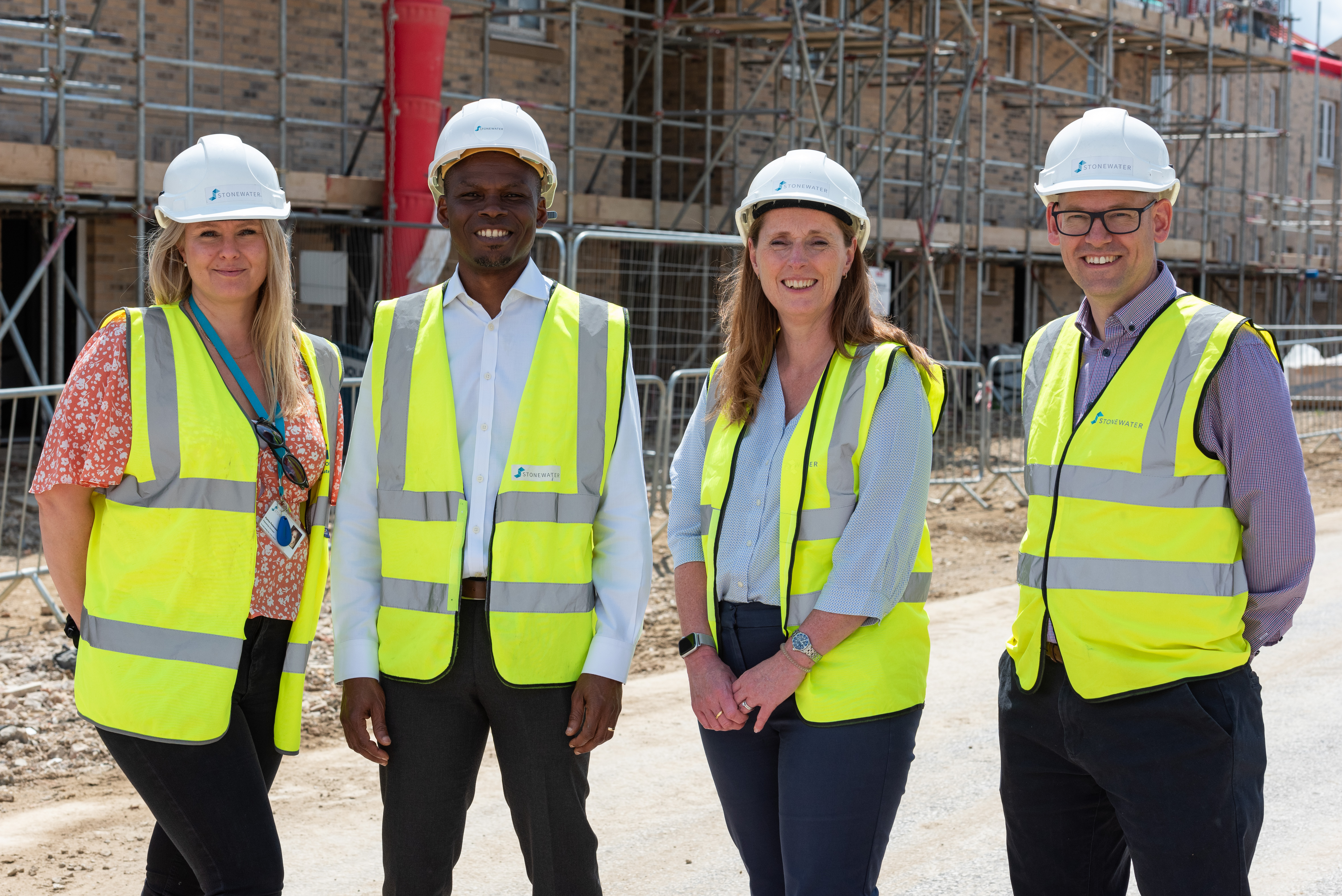 Four colleagues in hi-vis jackets and hard hats smiling and facing camera, stood at development site