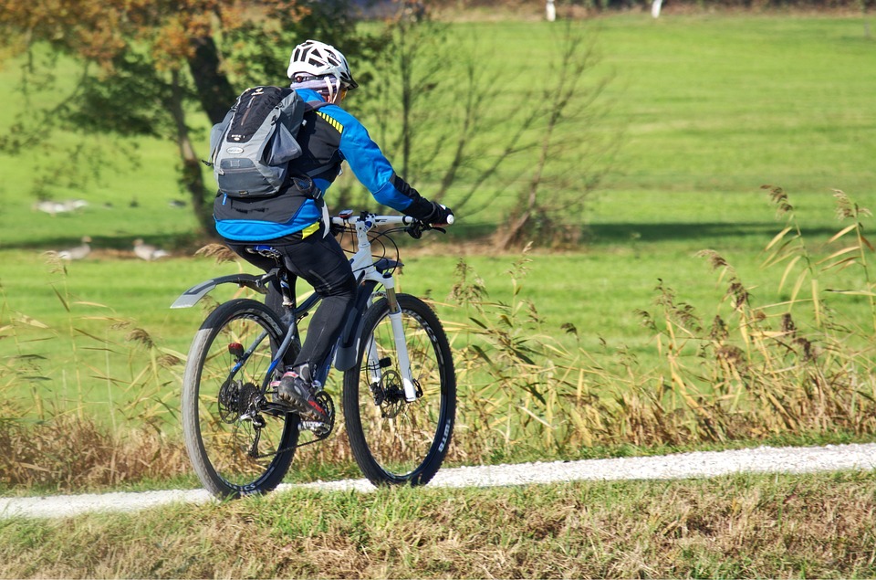 Man in cycling gear cycling on white stone path through a green space