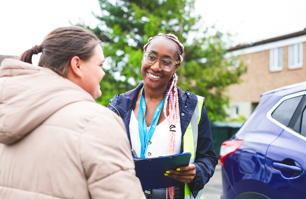 Two people talking, one holding a clipboard and smiling