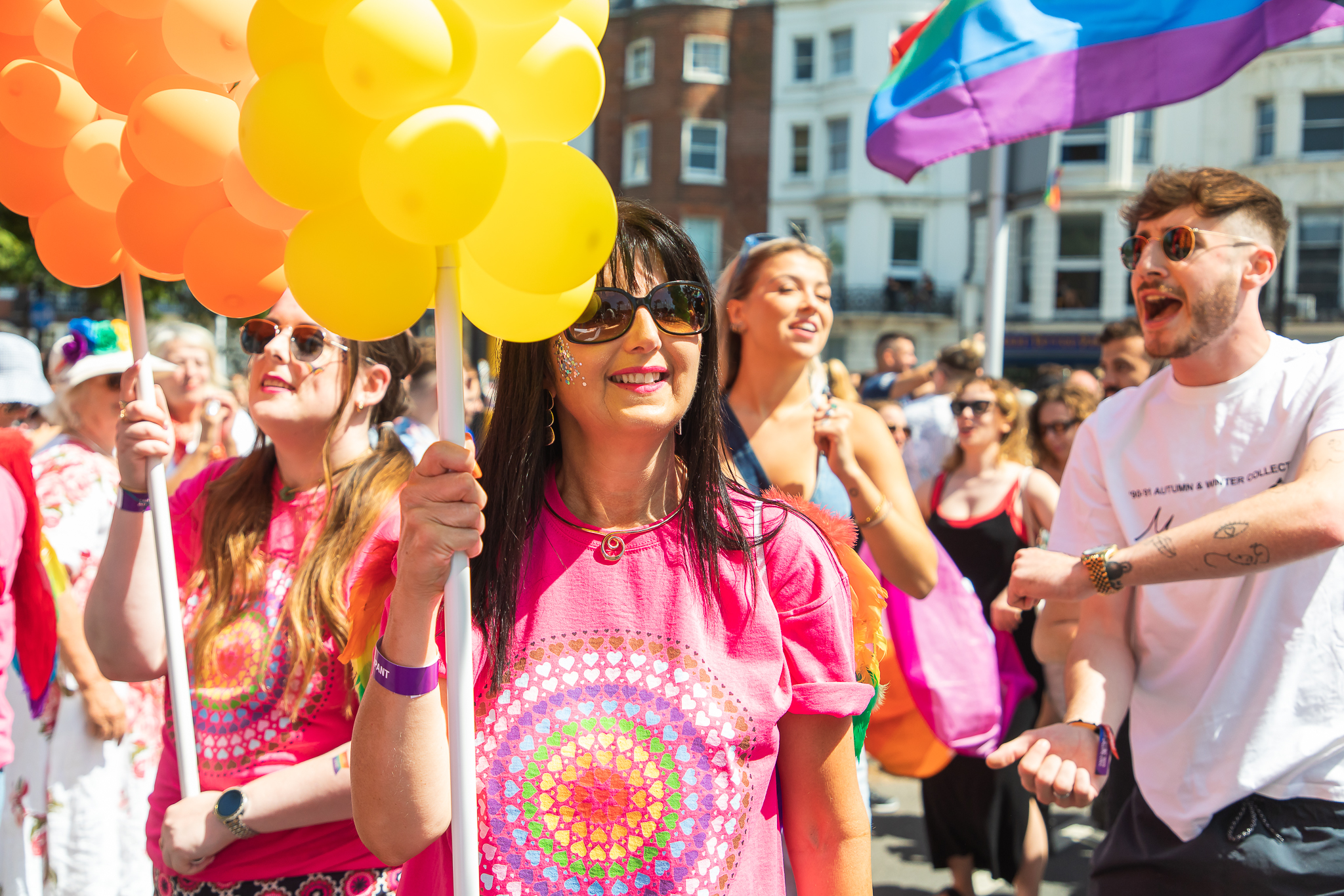 Stonewater colleague wearing pink Pride t-shirt, holding yellow balloons at Pride event