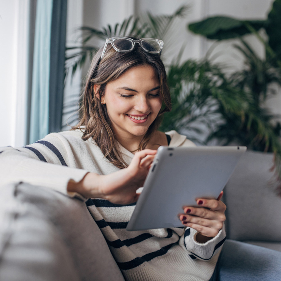Woman sitting on a sofa holding a tablet device smiling.