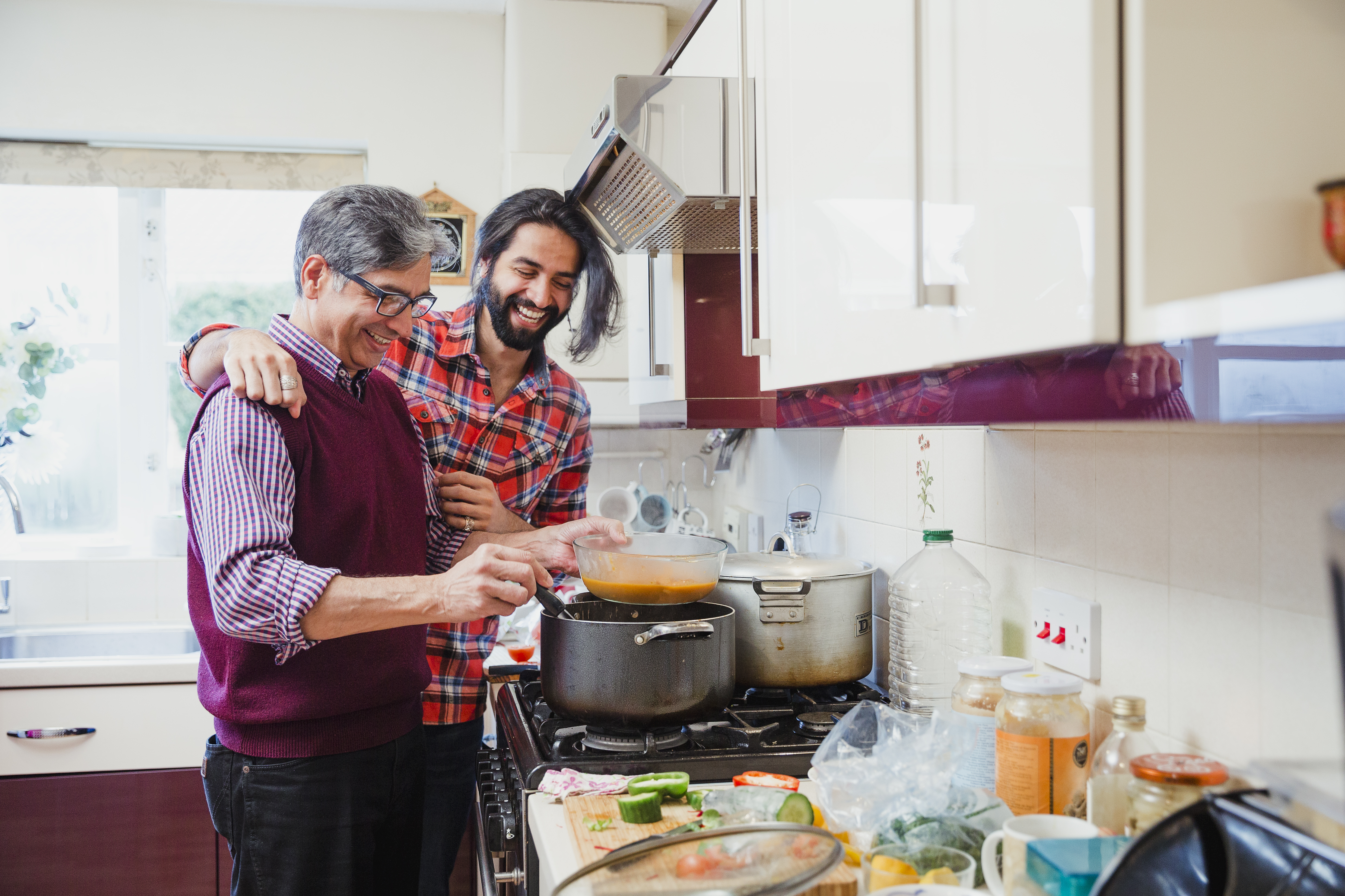 South-Asian father and son stood over a dish on the hob, cooking in kitchen