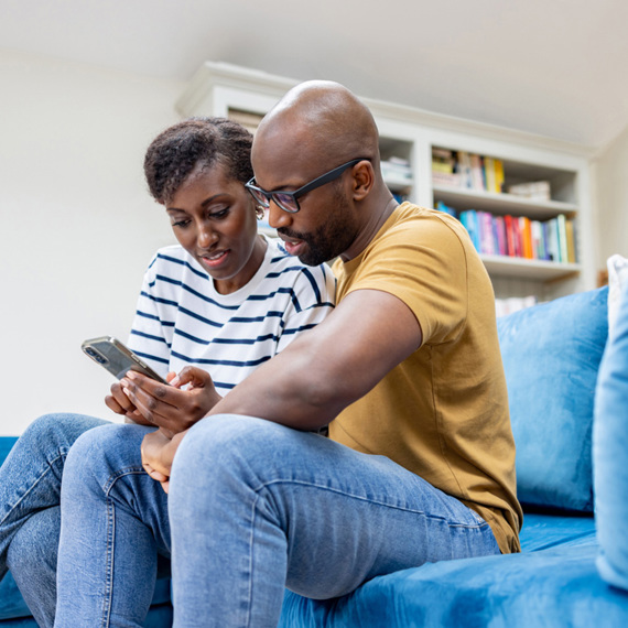 A man and a woman sat on a blue sofa looking at a phone together.