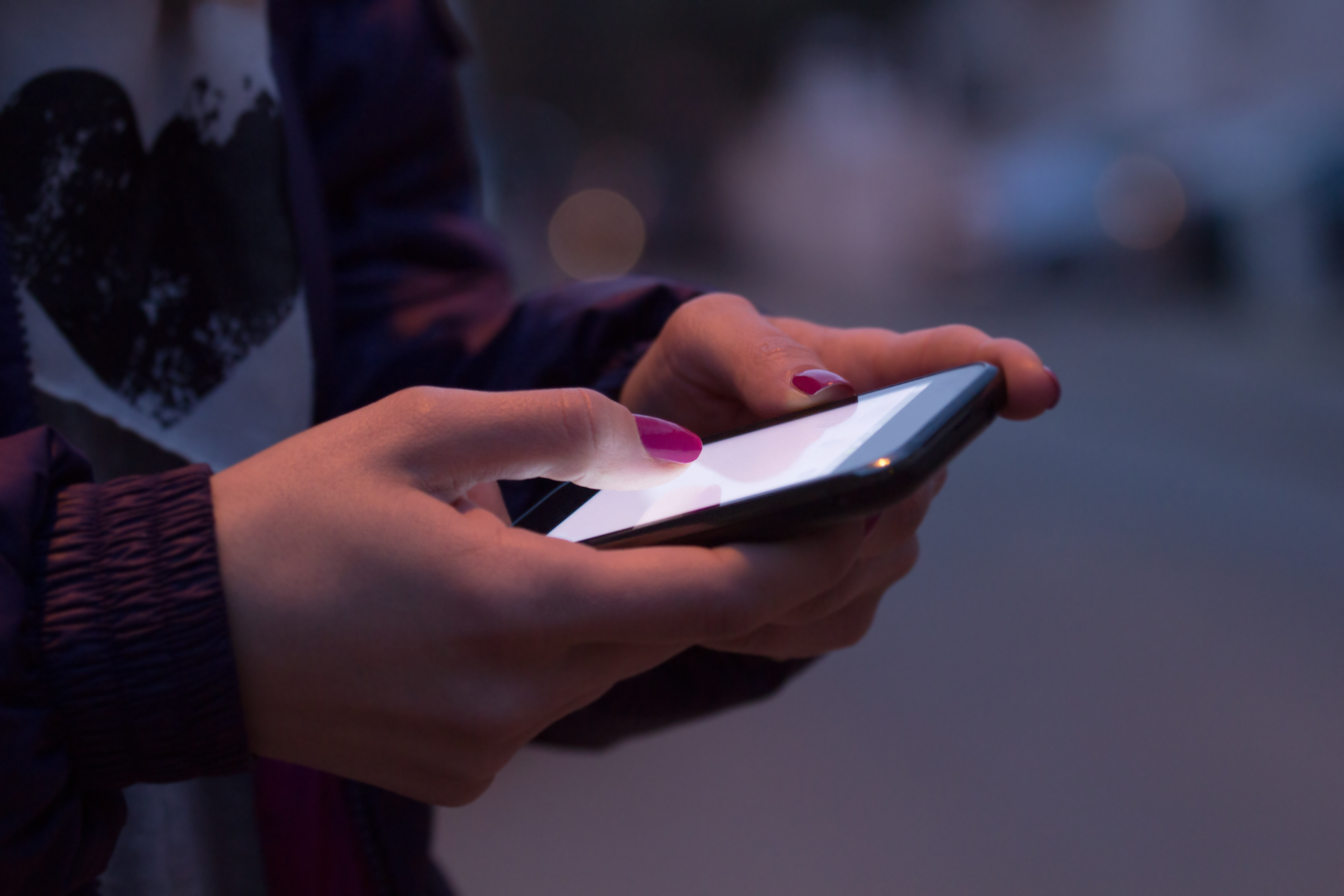 Close up of woman's hands with pink nails holding phone, stood outside at night