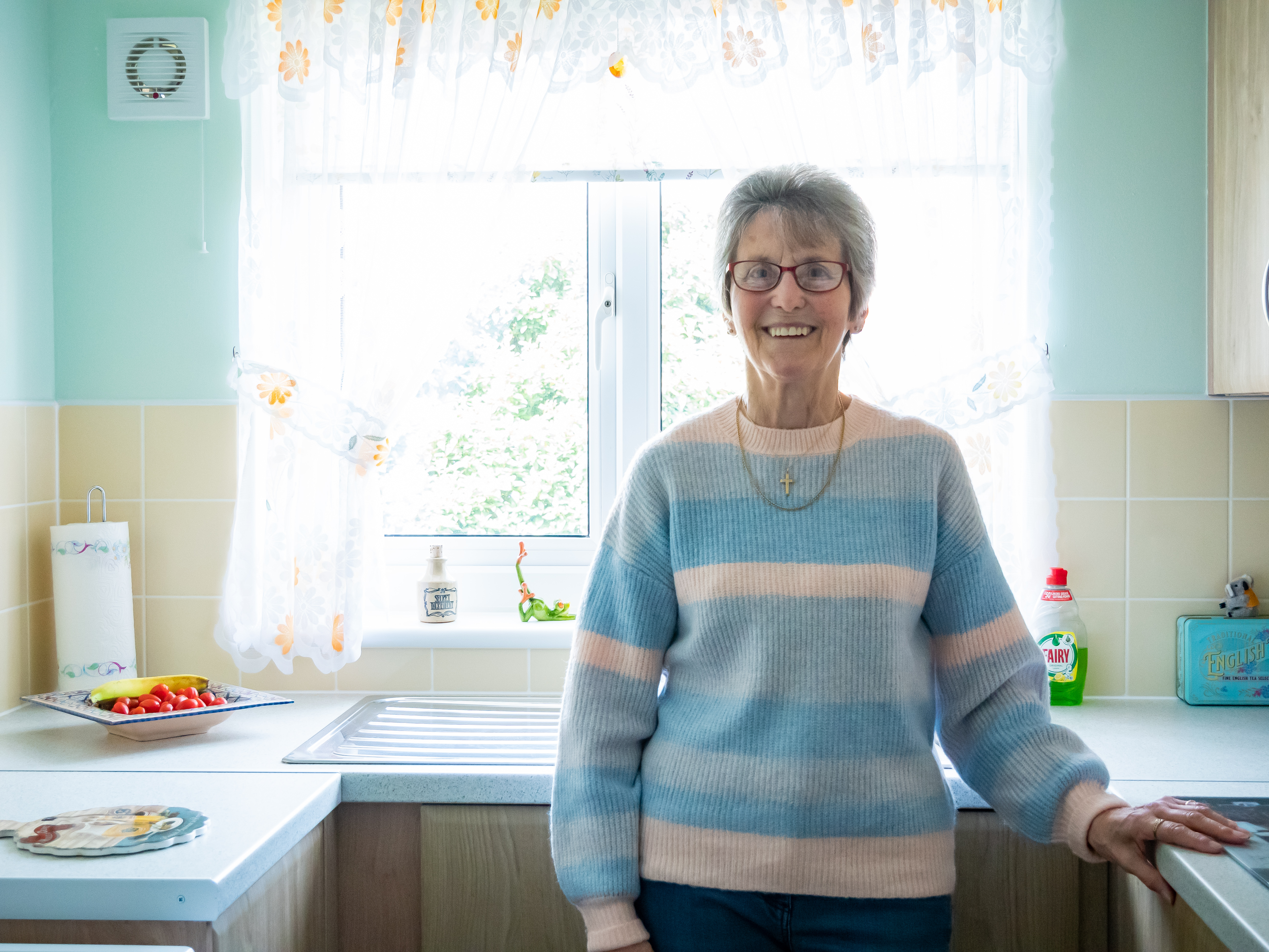 Elderly customer stood smiling in her kitchen