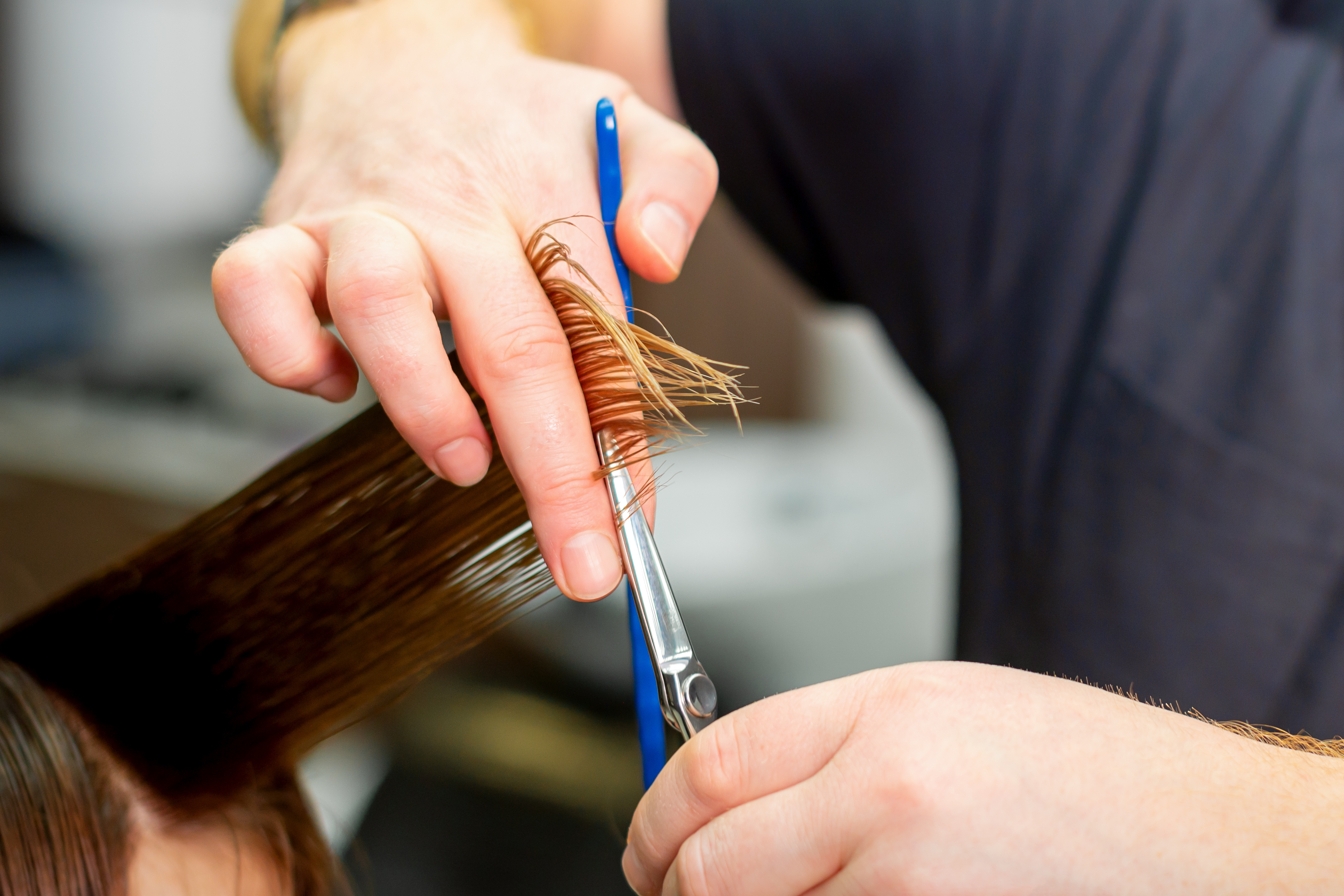 Close-up of a man cutting another person's hair with silver scissors