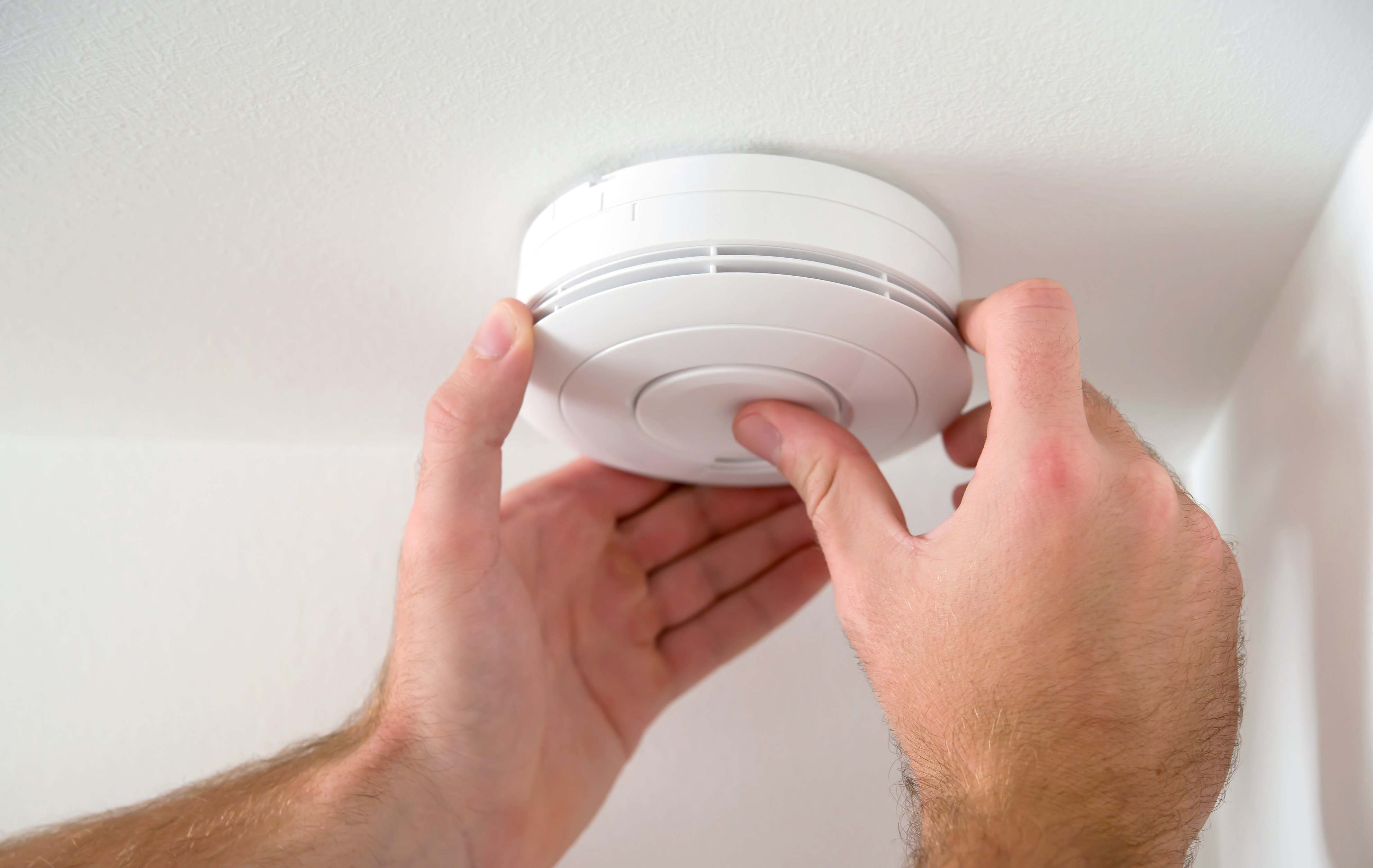Close-up of male hands testing a white fire alarm on a white ceiling